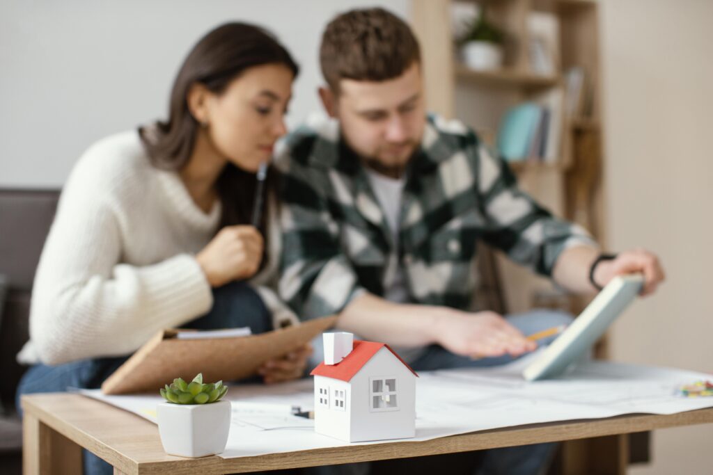 Un couple examine attentivement des documents de propriété et un ordinateur portable pour préparer une vente immobilière.